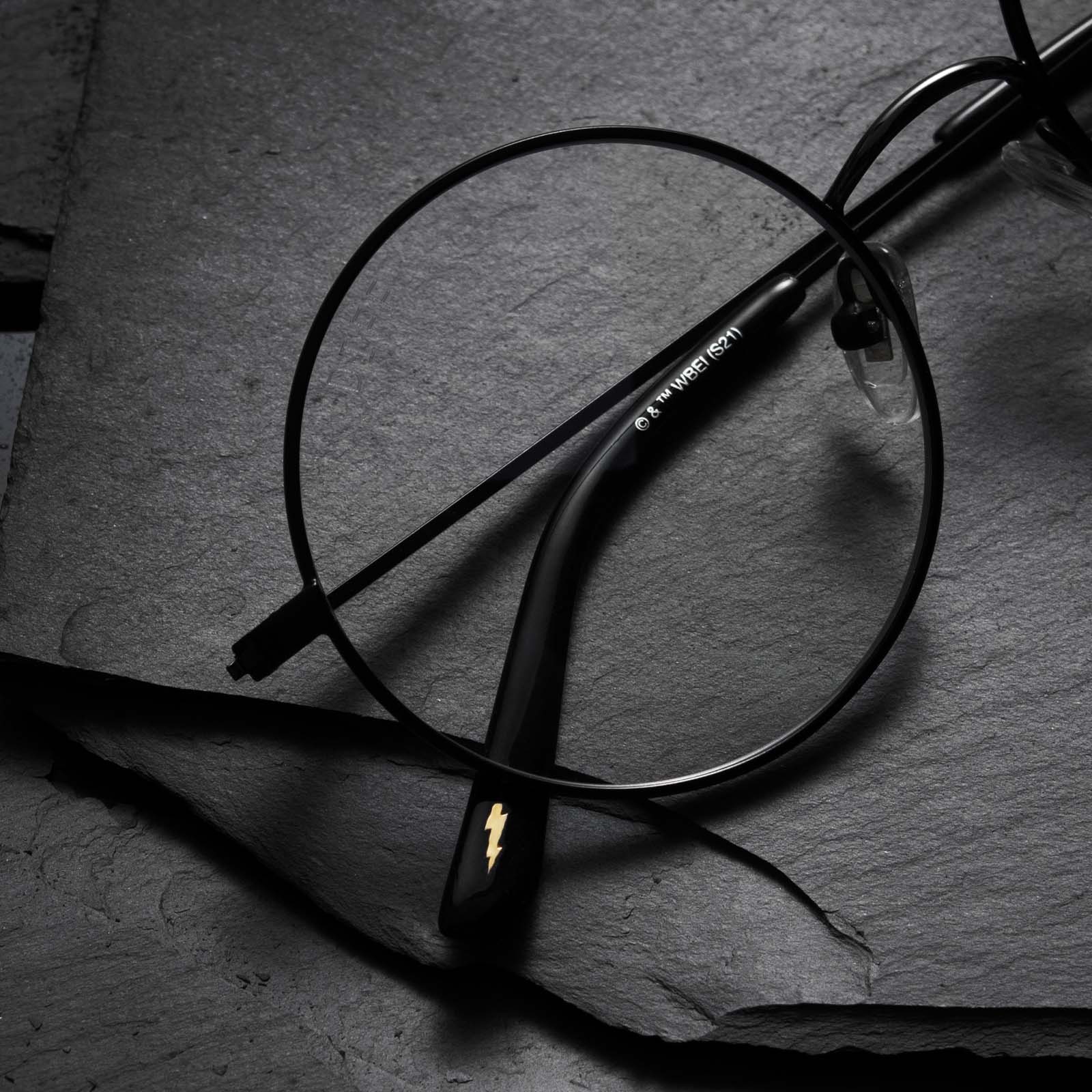 Close up of Harry Potter x DIFF Harry Potter glasses lying folded on top of black broken stone