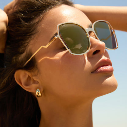 lifestyle - female wearing diff eyewear donna iii oversized square sunglasses with a gold metal frame and gold mirror polarized lenses angled view