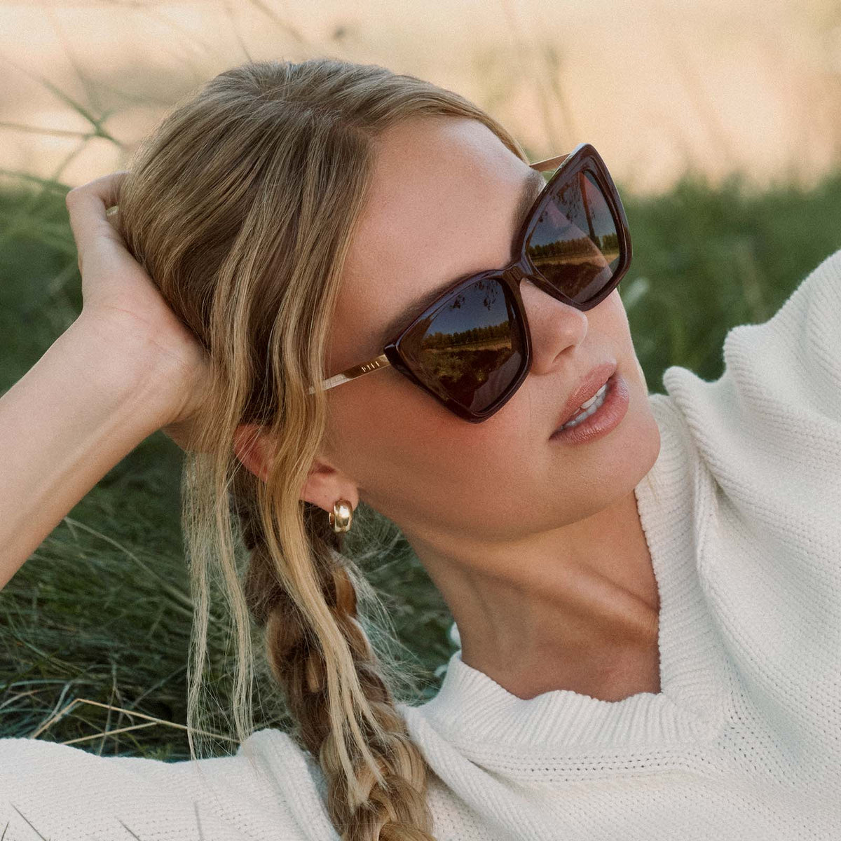 lifestyle - female wearing diff eyewear featuring the becky ii cateye sunglasses with a dark cherry lacquer frame and dark cherry gradient polarized lenses laying in the grass