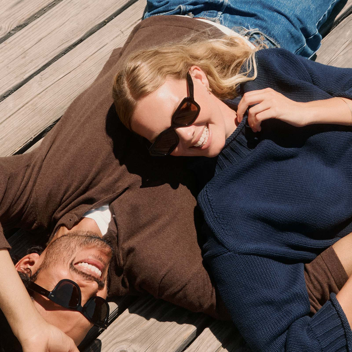lifestyle - blonde female laying on a deck wearing diff eyewear gwynn square sunglasses with a black acetate frame and brown polarized lenses angled view