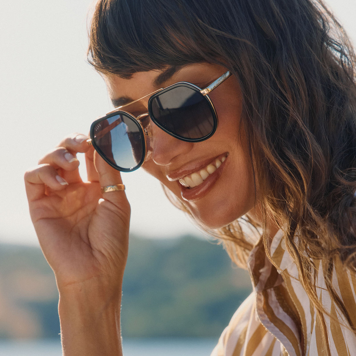 lifestyle - female wearing diff eyewear featuring the joey round sunglasses with a black & gold metal frame with grey gradient polarized lenses angled view