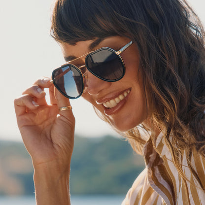 lifestyle - female wearing diff eyewear featuring the joey round sunglasses with a black & gold metal frame with grey gradient polarized lenses angled view