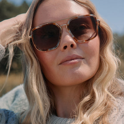 lifestyle - blonde female outdoors wearing diff eyewear jordan navigator sunglasses with a dove tortoise brown frame, gold temples, and brown gradient polarized lenses front view