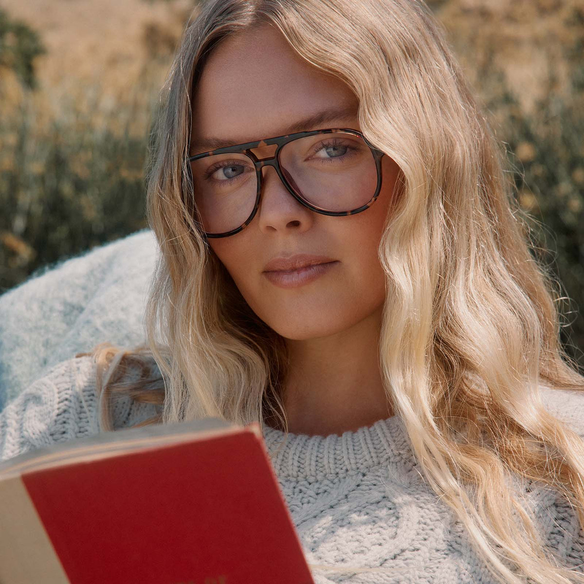 lifestyle - female in a park reading a book with diff eyewear featuring the tatum aviator blue light readers with a espresso tortoise frame front view