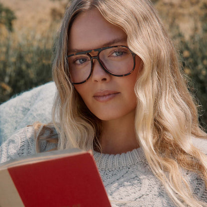 lifestyle - female in a park reading a book with diff eyewear featuring the tatum aviator blue light readers with a espresso tortoise frame front view