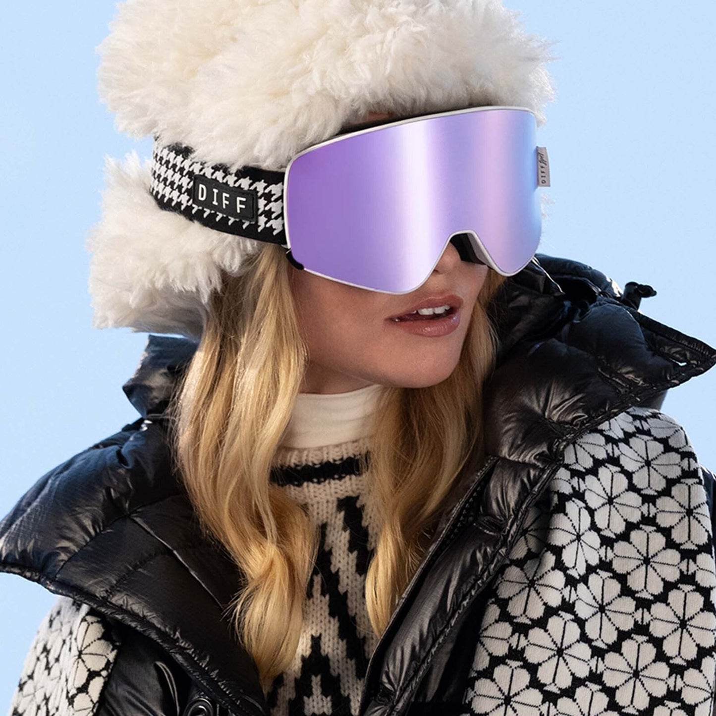 lifestyle - blonde model wearing purple snow goggles with black and white puffer jacket