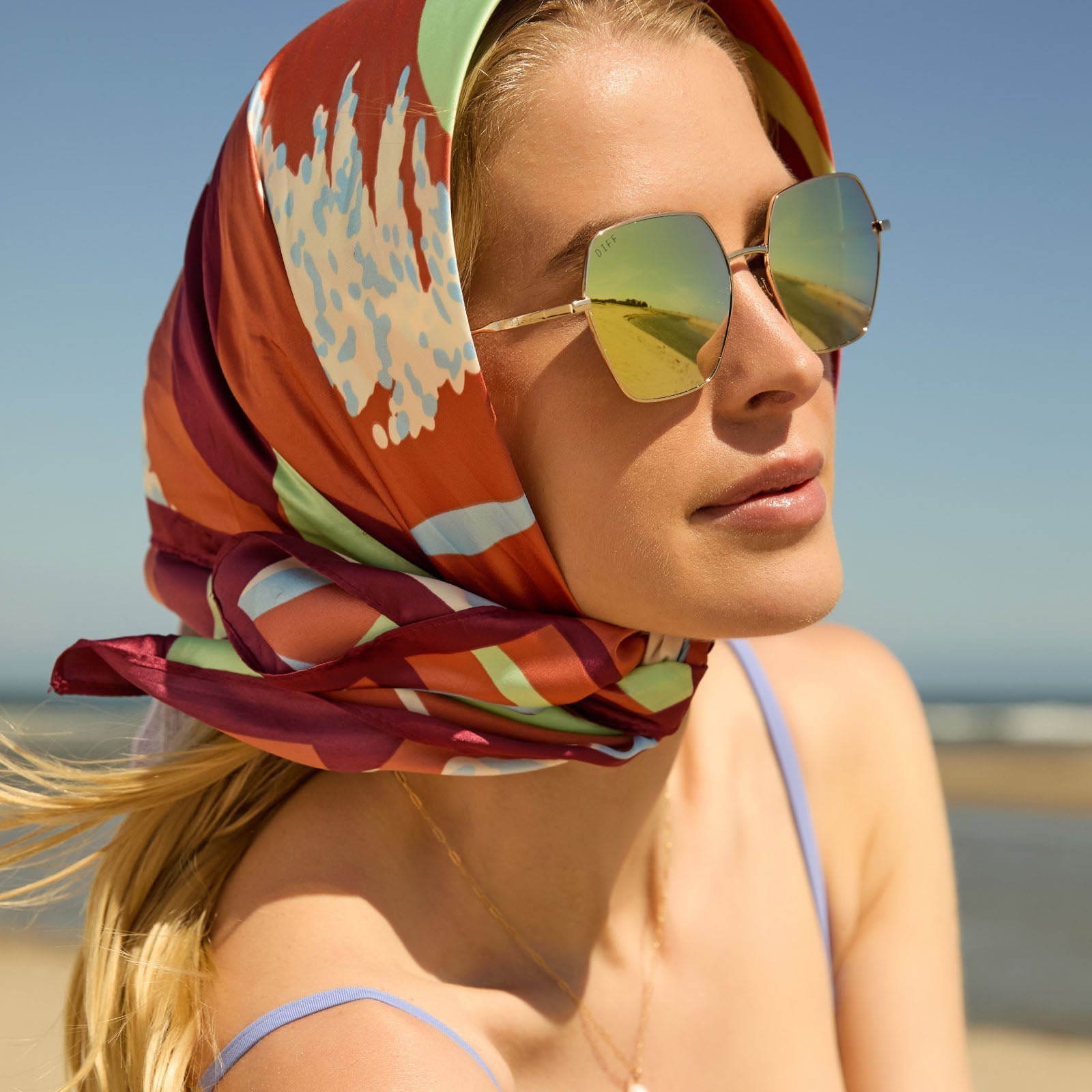 lifestyle - female at the beach wearing diff eyewear harlowe oversized square sunglasses with a gold metal frame and brilliant gold mirror lenses side view