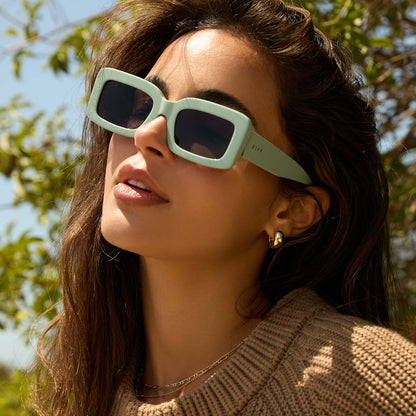 on model - female while at the beach wearing diff eyewear featuring the indy rectangle sunglasses with a steel teal frame and grey polarized lenses angled view