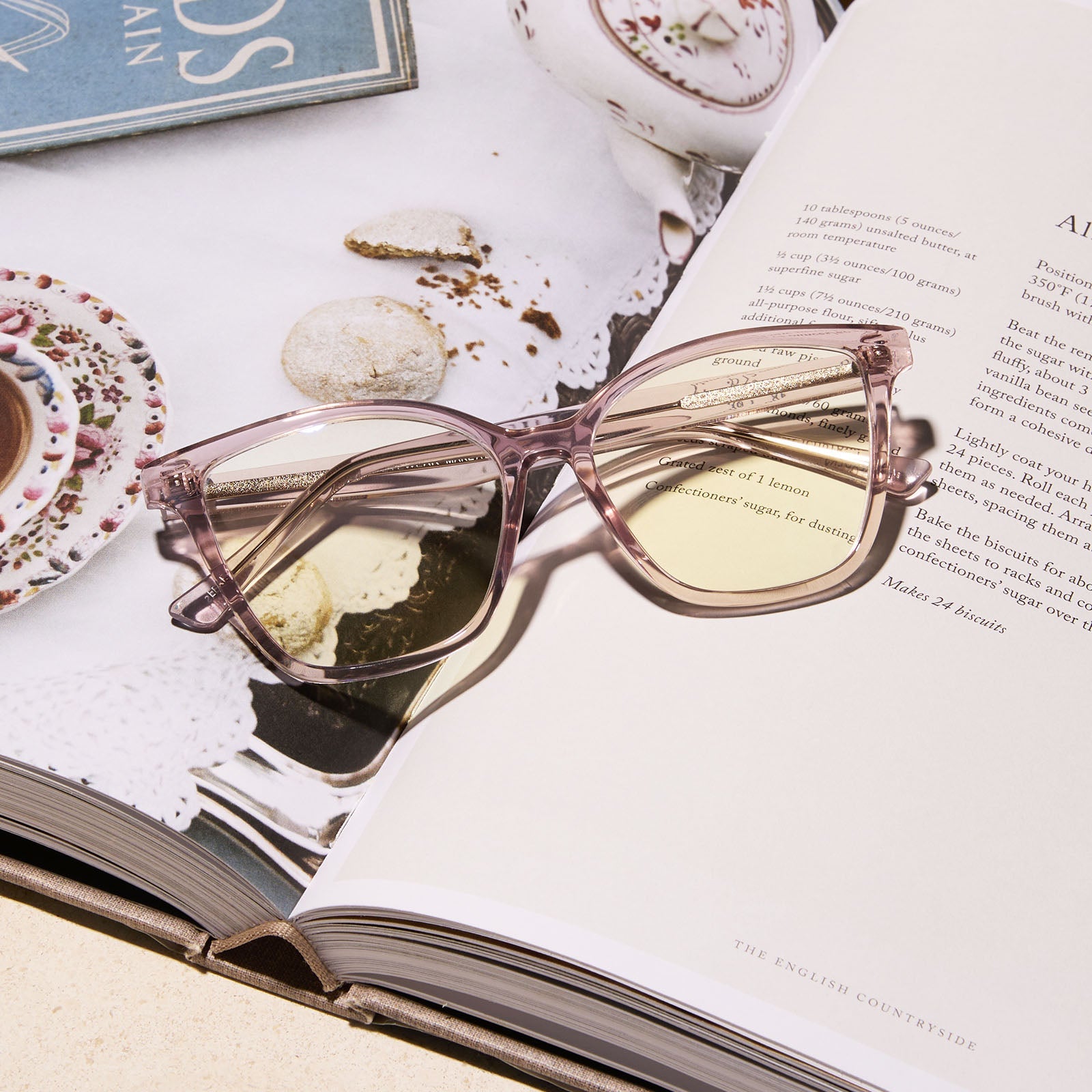 lifestyle - diff eyewear featuring the leah square blue light readers with a light pink crystal frame laying on a book