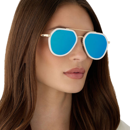 on model - female wearing diff eyewear featuring the joey round sunglasses with a snowbound & gold metal frame with blue mirror lenses angled view