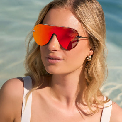 lifestyle - at the beach female wearing diff eyewear featuring the imani shield sunglasses with a gunmetal frame and red hot summer mirror lenses angled view