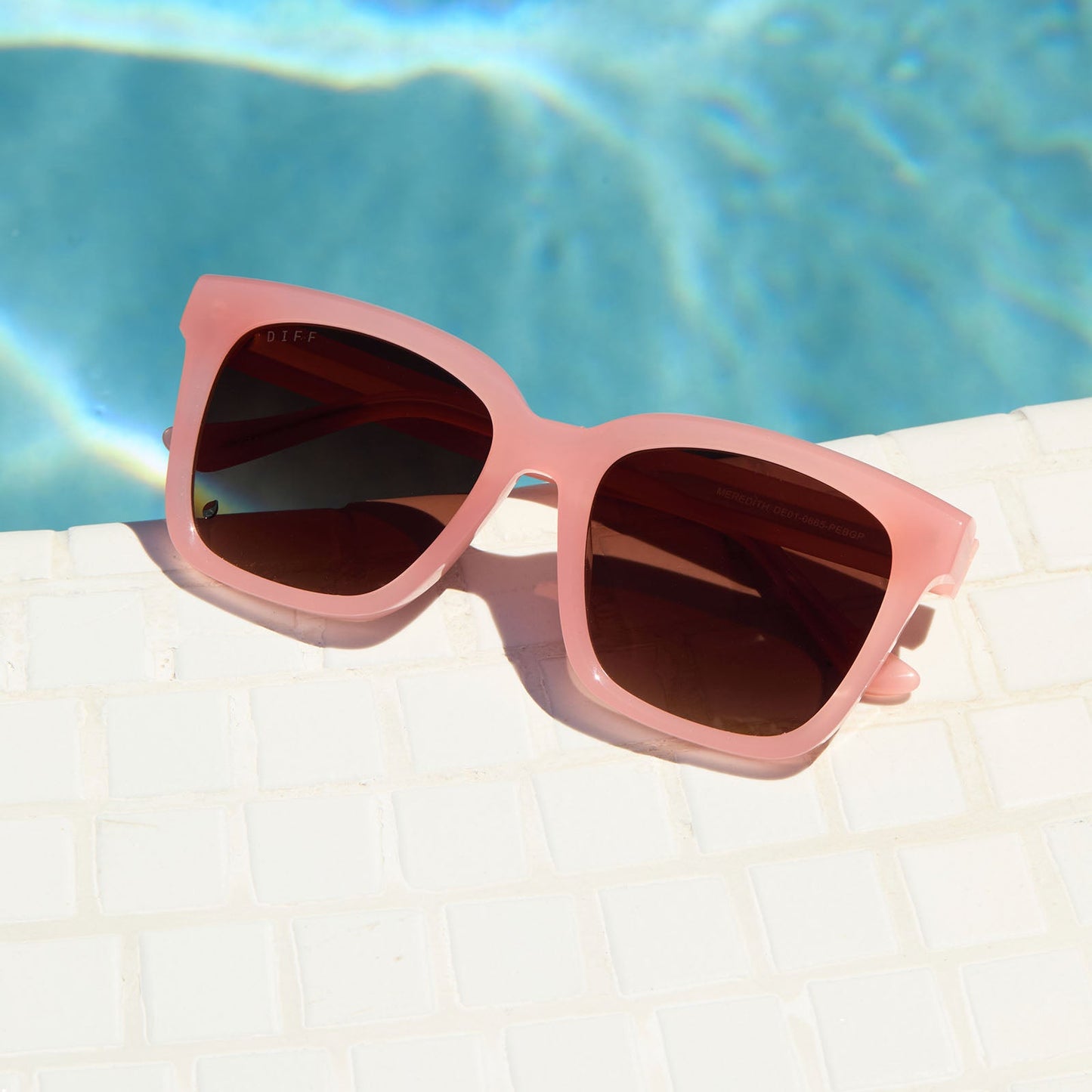 lifestyle - still life of diff eyewear meredith square sunglasses in peach laying by the pool