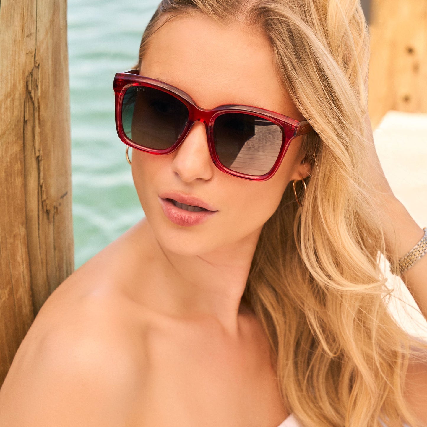 lifestyle - female wearing diff eyewear featuring the meredith square sunglasses with a red hot summer frame and grey gradient polarized lenses front view at the beach