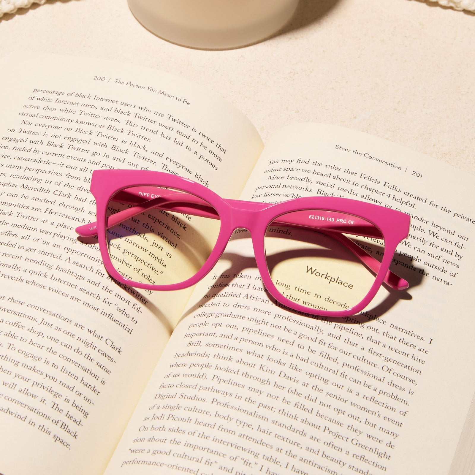 lifestyle - diff eyewear featuring the willa square blue light readers with a peony pink frame laying on an open book